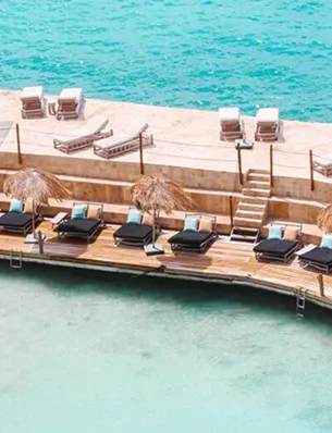 A private beach with sun loungers and straw umbrellas on a wooden pier and stone terraces, overlooking crystal-clear turquoise water, ideal for a luxury 5-star beachfront hotel in Guadeloupe.
