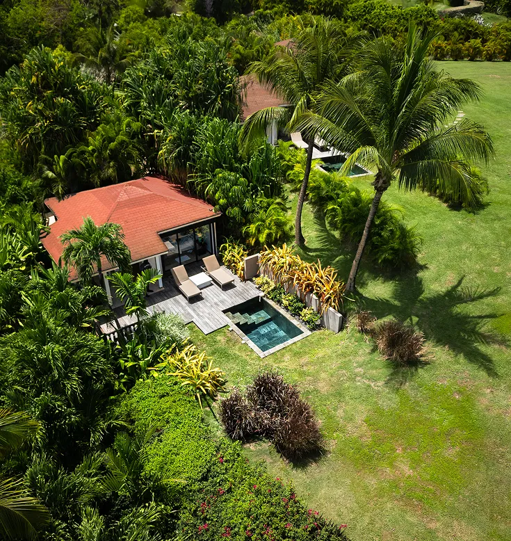 Aerial view of a luxury villa with a red roof, surrounded by lush vegetation, with a private pool and a wooden deck. Ideal for renting a villa with pool in Guadeloupe.