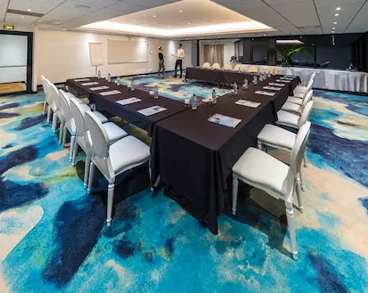 Spacious and modern meeting room arranged in a U-shape, with black tables and white chairs, on a carpet with blue and turquoise patterns, perfect for conferences in a hotel in Guadeloupe.