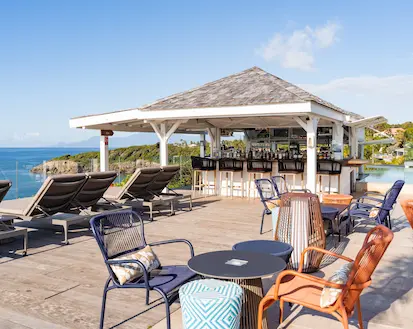 An outdoor cocktail bar with a wooden roof and varied seating, overlooking an infinity pool and the Caribbean Sea. An ideal setting for a 5-star luxury hotel in Guadeloupe.