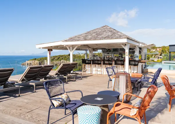 An outdoor cocktail bar with a wooden roof and varied seating, overlooking an infinity pool and the Caribbean Sea. An ideal setting for a 5-star luxury hotel in Guadeloupe.