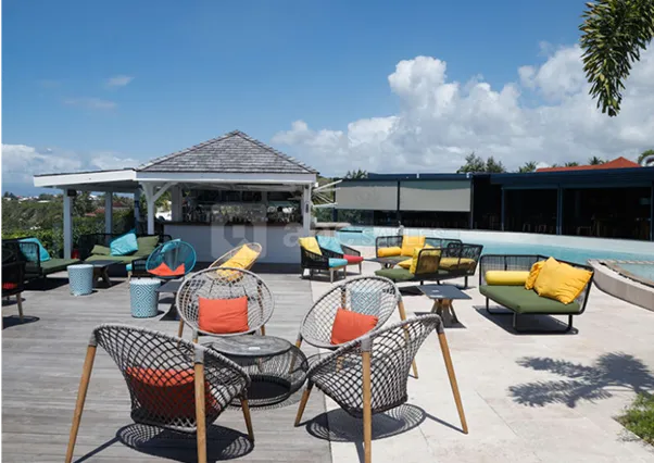 Outdoor cocktail bar area of a luxury hotel in Guadeloupe, with colorful armchairs and sofas, a swimming pool and sea views, ideal for relaxing under the Caribbean sun.