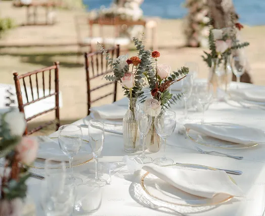 Elegantly set wedding table with flowers, cutlery and glassware, on a sandy beach in the background, ideal for a Caribbean wedding in Guadeloupe.