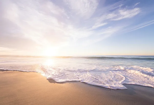 A golden sandy beach with waves foaming under a partly cloudy sky at sunset or sunrise, ideal for a beach hotel or a seaside wedding in Guadeloupe.