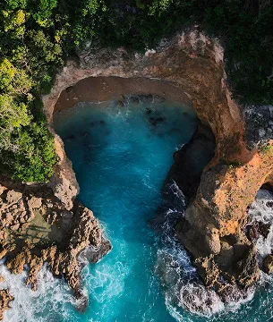 Aerial view of a natural rock formation in the shape of a heart on the coast of Guadeloupe, with a turquoise water cove and green cliffs, a unique place overlooking the sea.