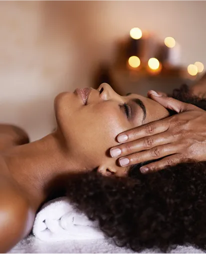 Close-up of a woman with her eyes closed receiving a facial massage or facial treatments, with fuzzy candles in the background, symbolizing a relaxing experience at a luxury spa in Guadeloupe.
