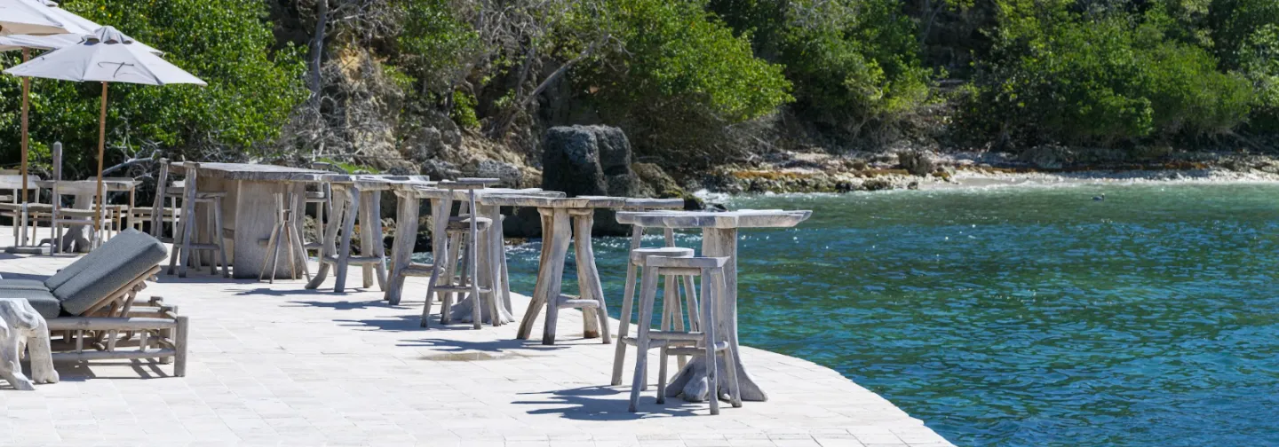 Two daybeds with colorful cushions on a wooden deck, offering panoramic views of the Caribbean Sea through a glass railing. Ideal for a luxury hotel or a villa overlooking the sea in Guadeloupe.