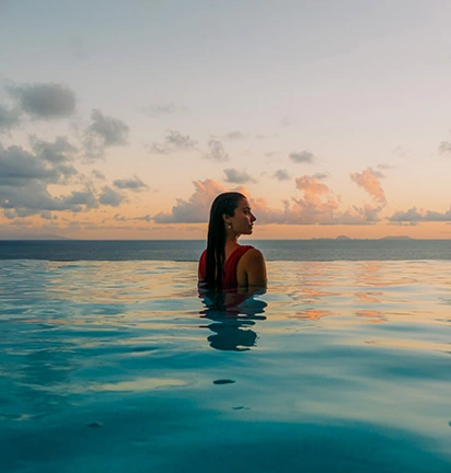 Woman relaxing in an infinity pool facing the ocean, at sunset in the Islands of Guadeloupe.