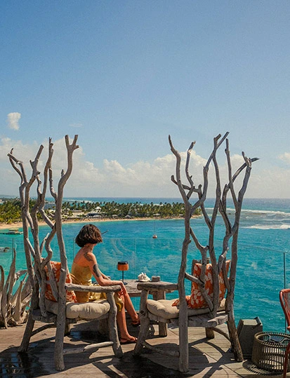 Femme assise sur une terrasse en bois face à la mer turquoise et aux palmiers à La Toubana Hôtel & Spa en Guadeloupe