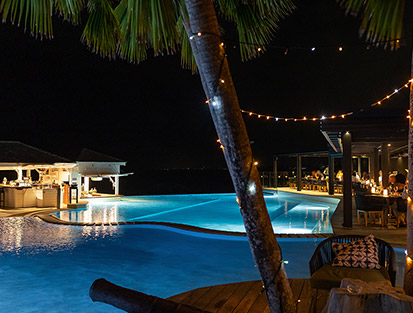 Illuminated swimming pool at night with bar and lively terrace at La Toubana Hotel & Spa in Guadeloupe.