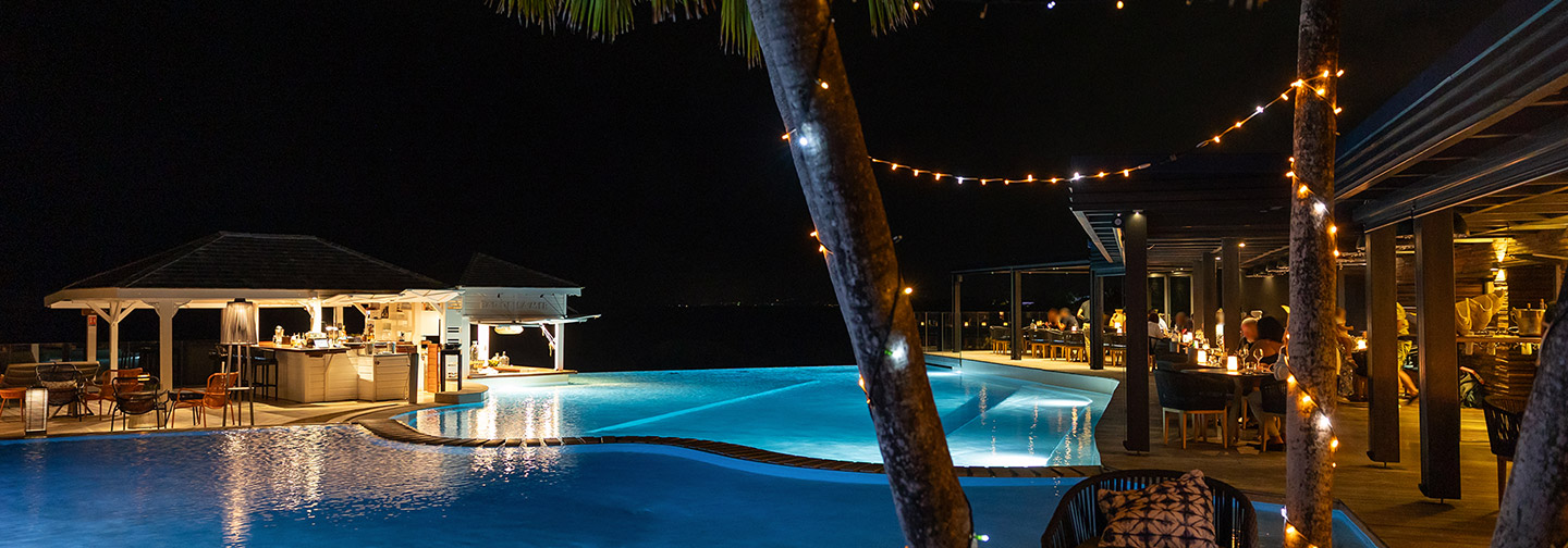 Piscine illuminée de nuit avec bar et terrasse animée à La Toubana Hôtel & Spa en Guadeloupe.