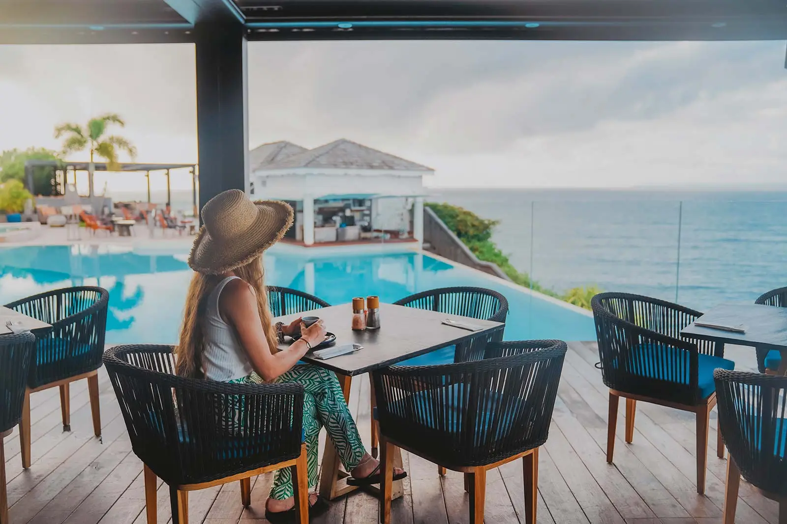 Femme prenant un café en terrasse face à la piscine et à la mer à La Toubana Hôtel & Spa en Guadeloupe