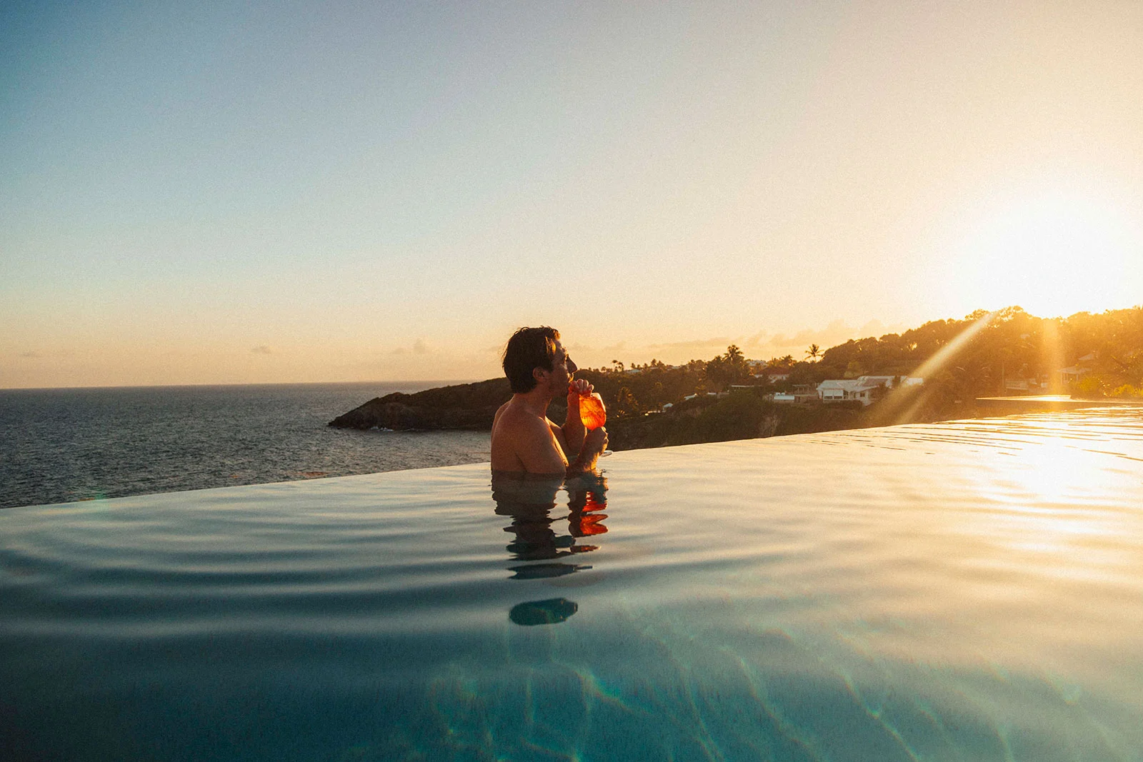 Homme se relaxant dans la piscine à débordement de La Toubana Hôtel & Spa au coucher du soleil, face à la mer en Guadeloupe