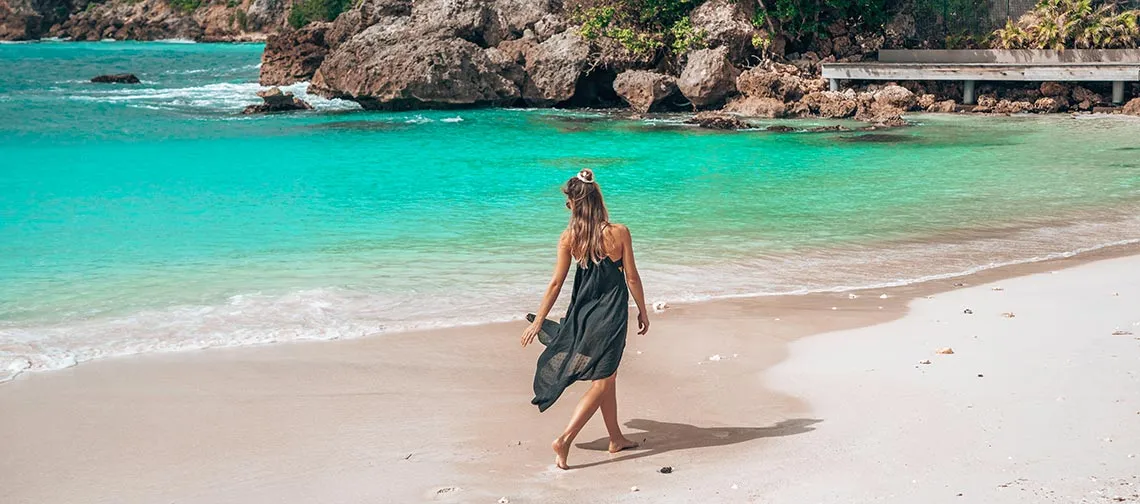 Femme marchant sur une plage turquoise en Guadeloupe, ambiance détente et évasion