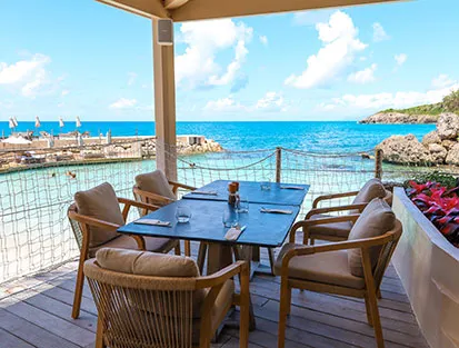 Mesa puesta en la terraza de madera del restaurante frente al mar turquesa en La Toubana Hotel & Spa en Guadalupe