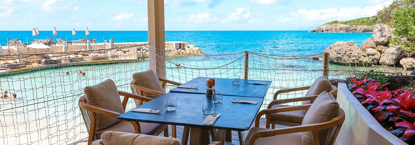 Mesa puesta en la terraza de madera del restaurante frente al mar turquesa en La Toubana Hotel & Spa en Guadalupe