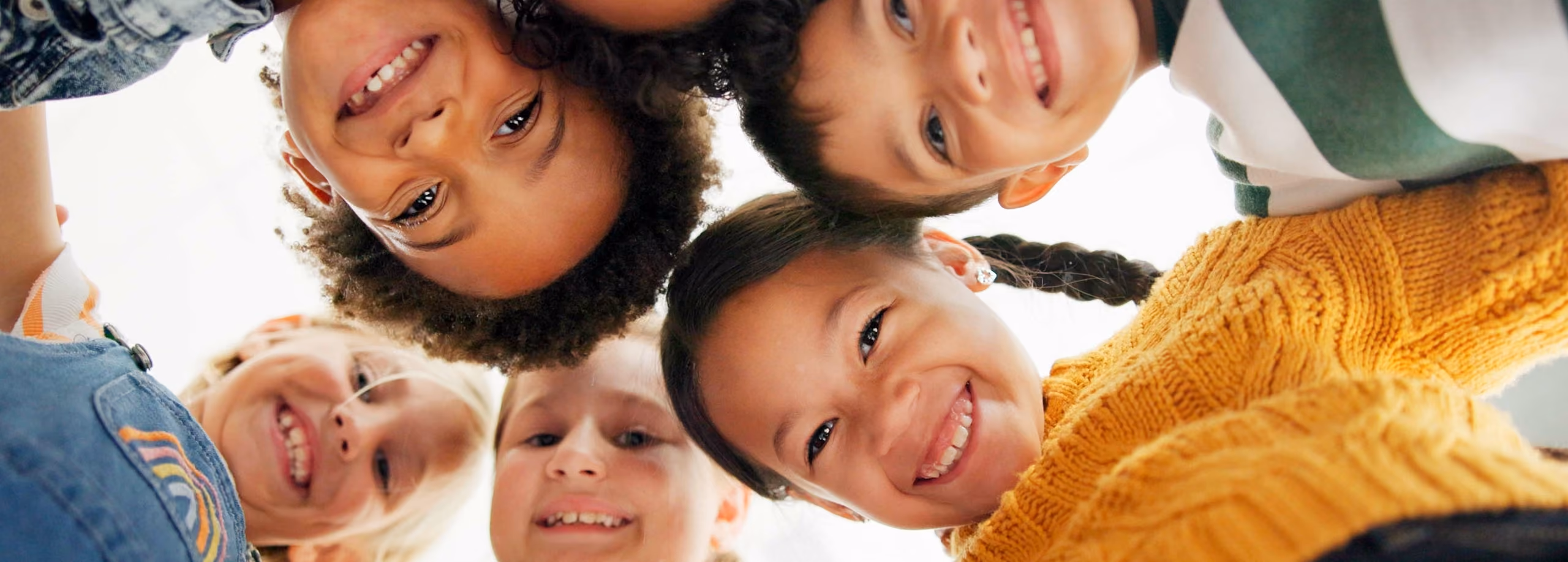 Group of five happy children smiling and looking down at the camera in a circle.
