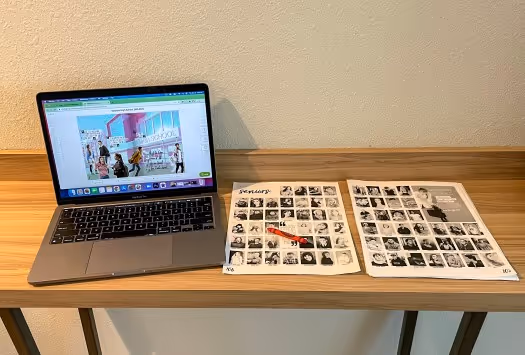 Laptop open to a yearbook spread with a PDF proof next to it for tracking coverage