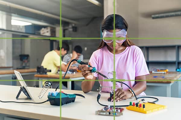 African American High School teenage Student wearing protective goggles soldering electronics circuit in the science technology workshop with overlay of rule of thirds to show the photography lesson of composition
