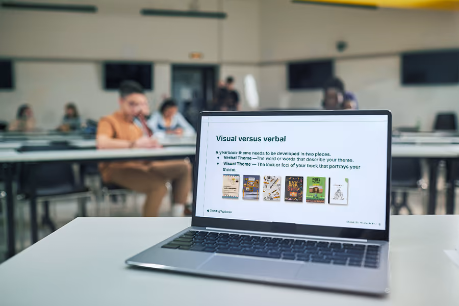 Laptop on desk showing a presentation slide about yearbook visual versus verbal themes in a classroom.
