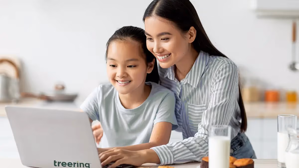 Smiling woman and girl looking at a laptop together in a kitchen with milk and snacks nearby.