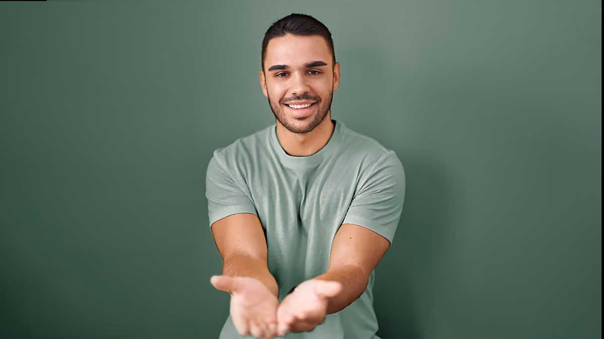 Smiling man in green shirt with outstretched hands on green background.