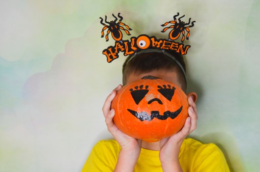 Young boys poses for the yearbook with a pumpkin at his classroom Halloween party for promotion of book sales.