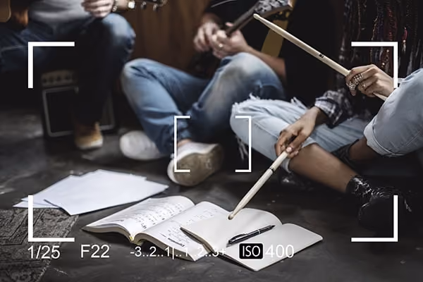 Musicians sitting on floor practicing with notebooks, sheet music, and drumsticks visible.