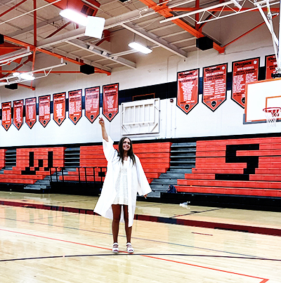 Graduation photo of a woman in a cap and gown throwing her cap in the air