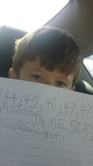 Kindergarten boy holding a paper with numbers to track howe many signatures are in the yearbook his mom made
