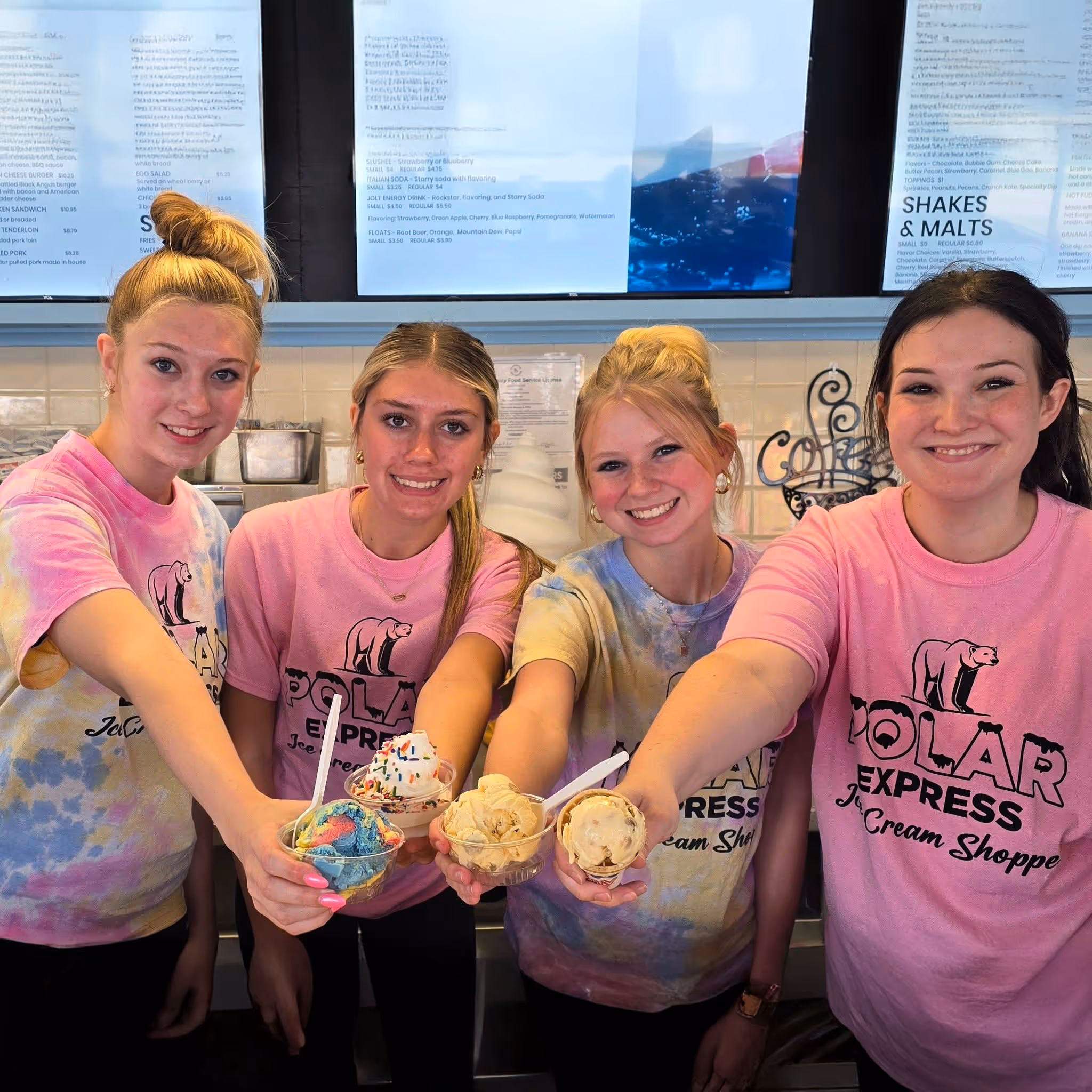 Four girls joyfully hold ice cream cups at an ice cream shop.