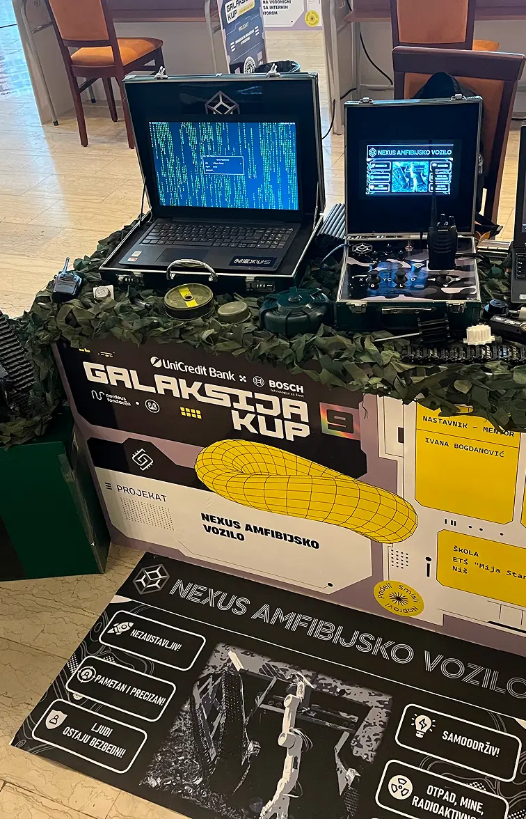 Izložbeni sto sa dva kompjutera u koferima, vojnim rekvizitima i natpisom Galaksija kup 9 i Nexus amfibijsko vozilo.
