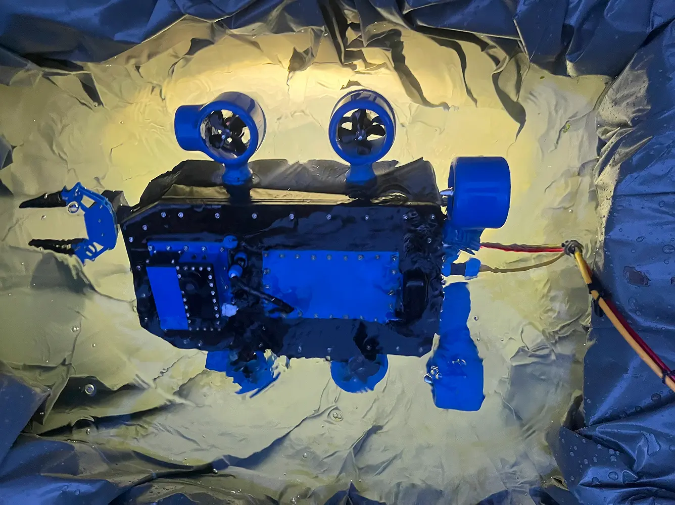 Plavi daljinski upravljani robot pod vodom sa propelerskim motorima i hvataljkom.