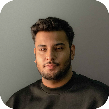 Portrait of a young man with short dark hair and a beard, wearing a dark shirt, smiling slightly against a dark background.