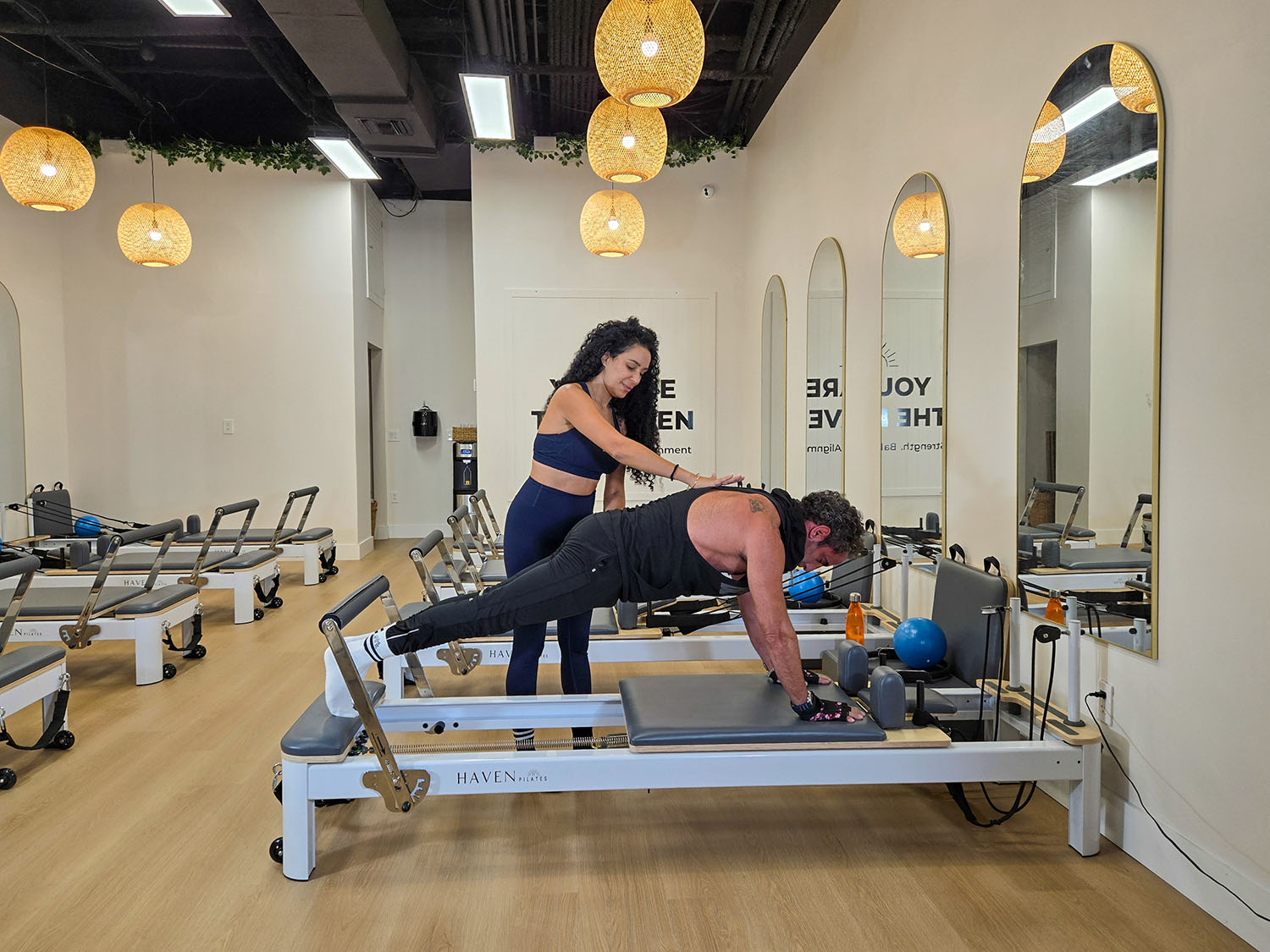 A female Pilates trainer holding the back of a trainee while he performs a Pilates exercise.