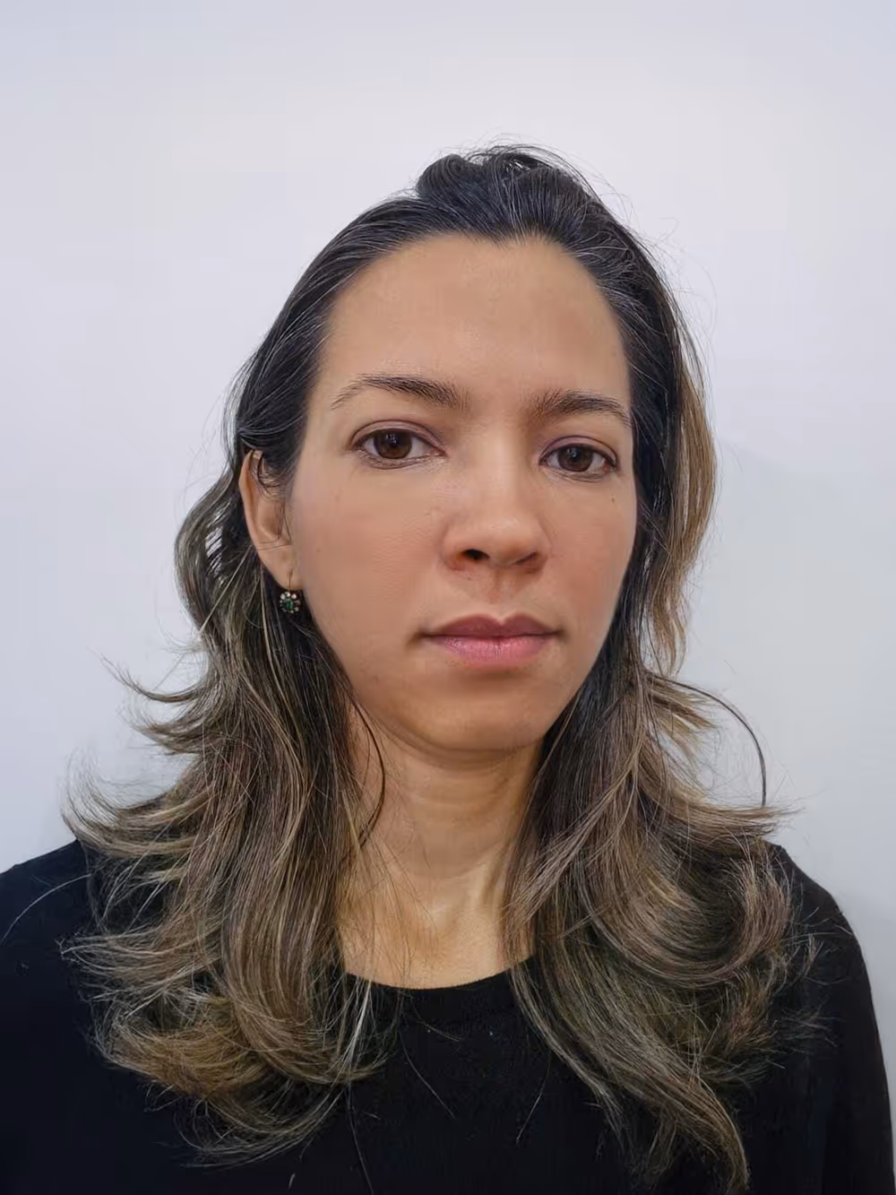 Woman with long wavy brown hair wearing a black shirt against a plain white background.
