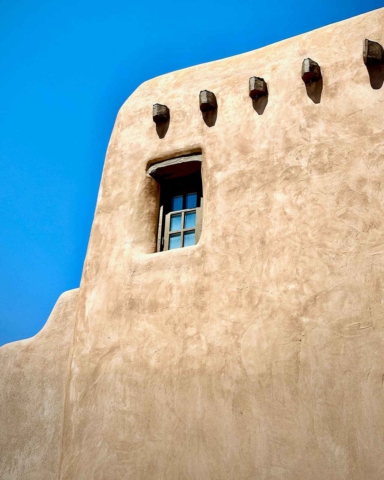 A close-up of a traditional Santa Fe adobe exterior under a clear blue sky, representing the appeal of modern luxury new construction in Santa Fe.