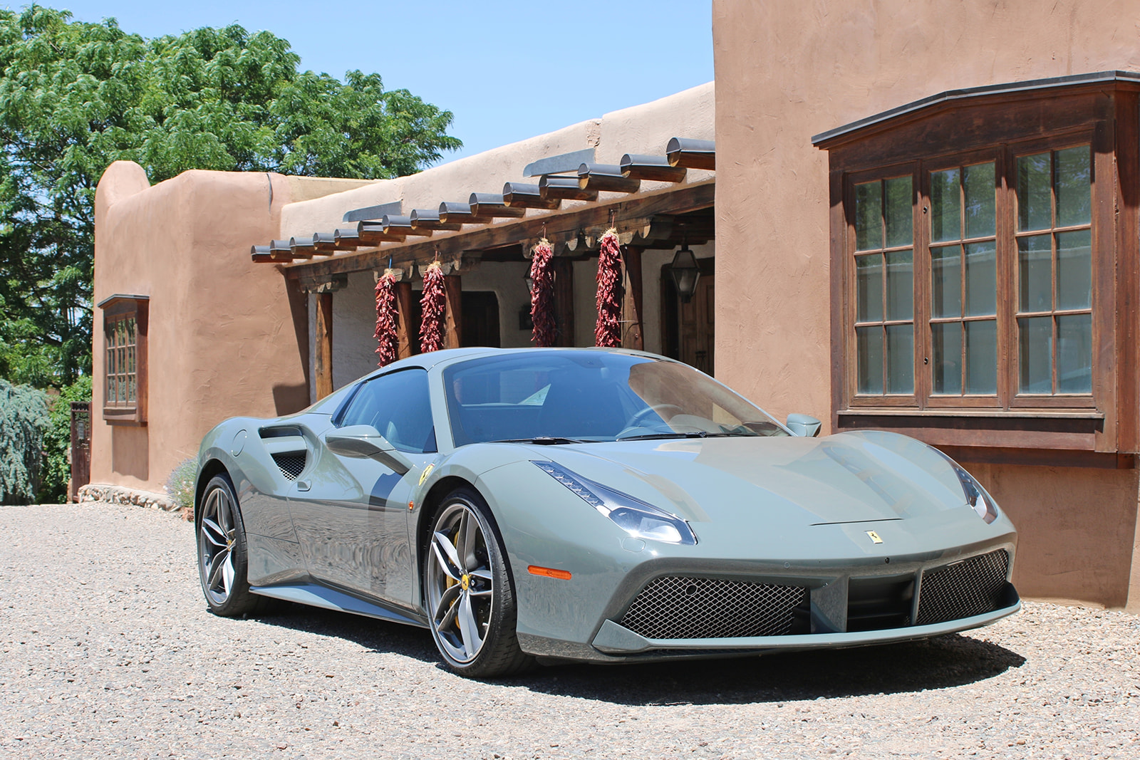 Gray Ferrari sports car parked on gravel in front of a southwestern-style adobe building with hanging red chili peppers.