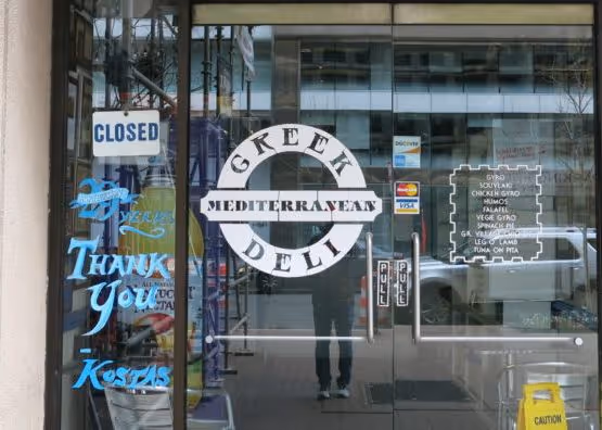 A man standing in front of a Greek deli.