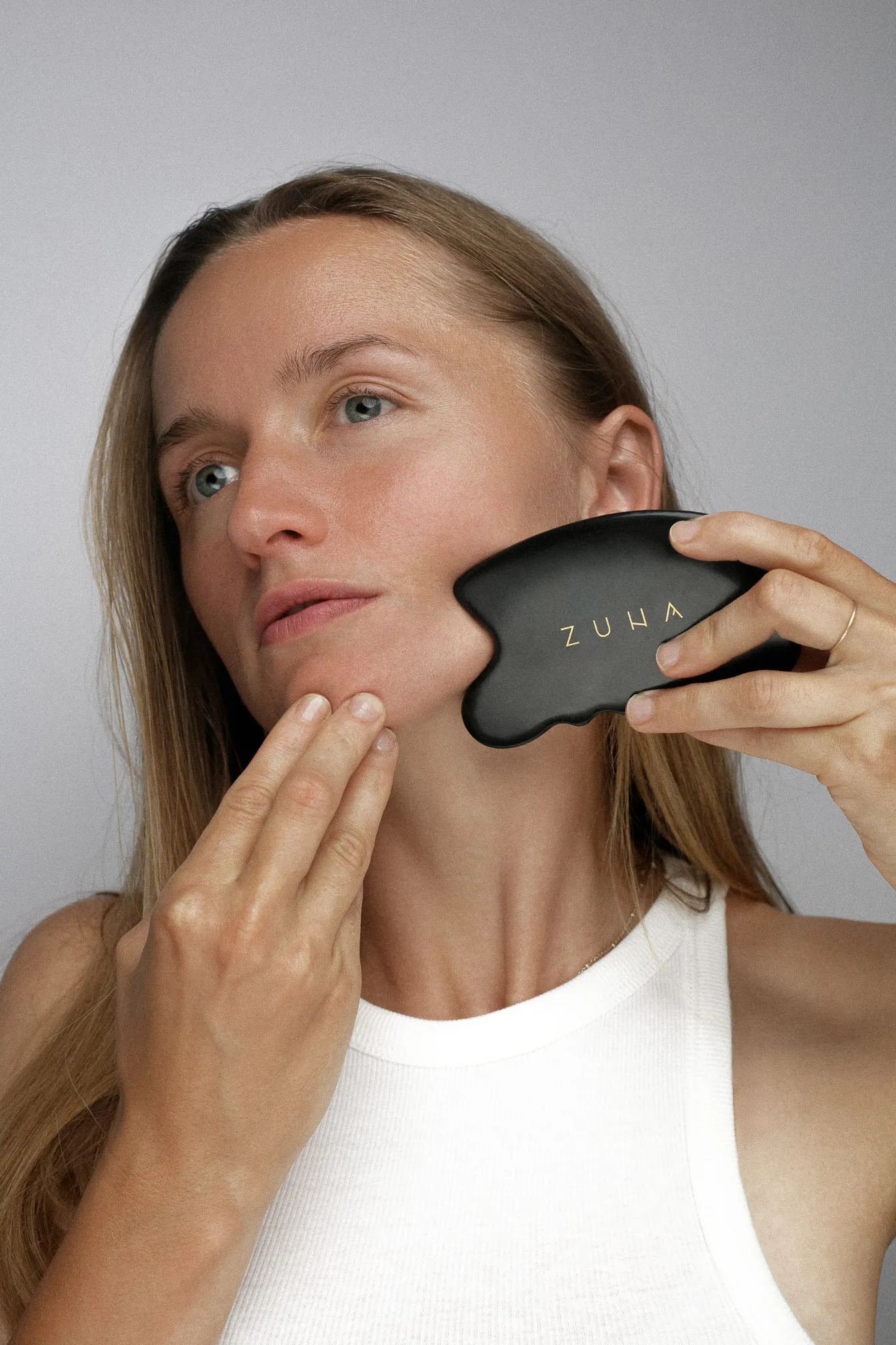 Žena masíruje tvár masážnym kameňom Zuna gua sha.