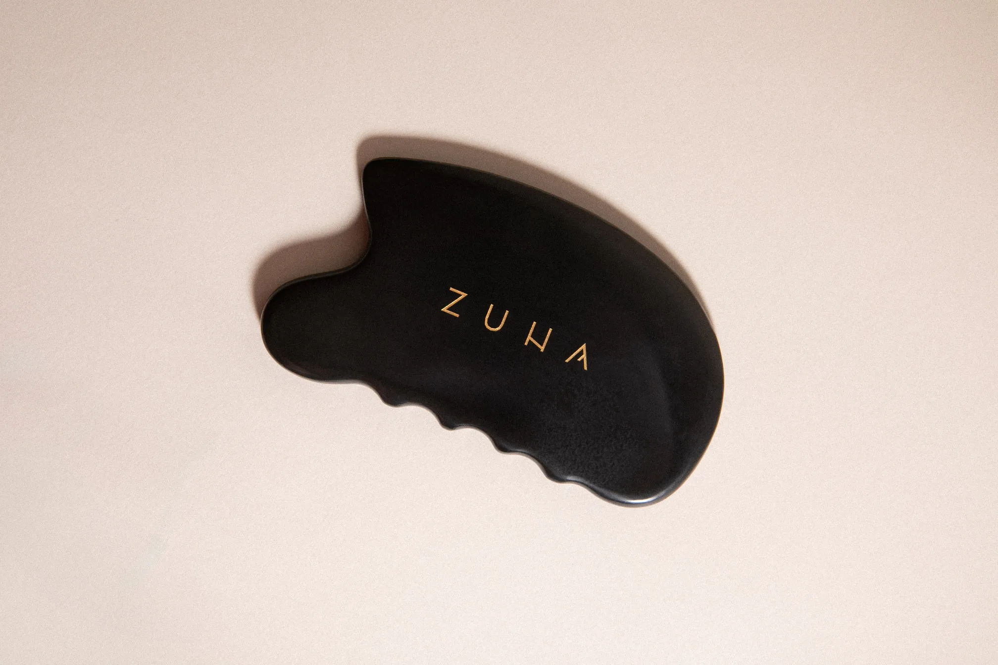 Zuna gua sha masážny kameň na krémovom podklade.