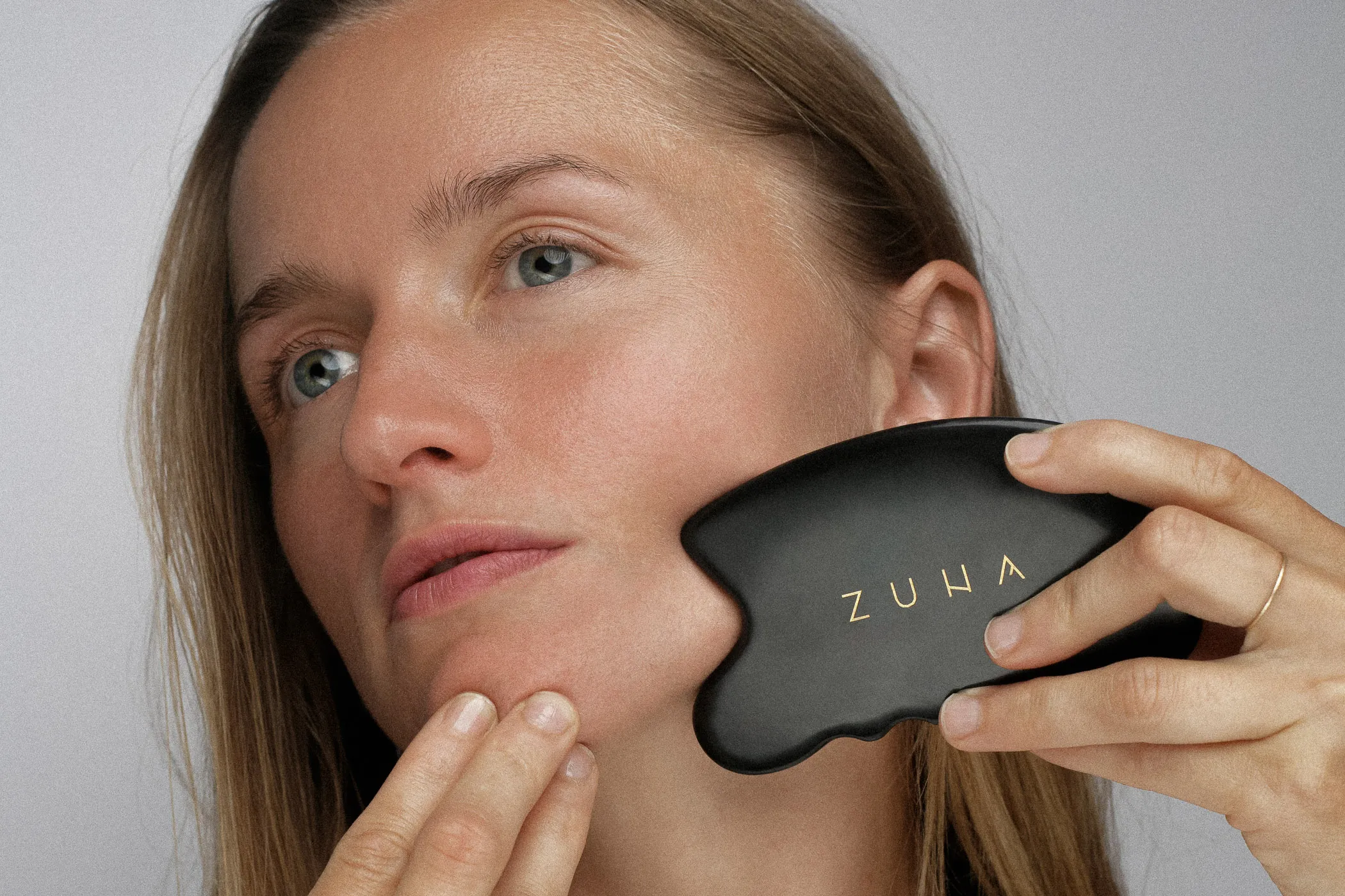 Žena masíruje tvár masážnym kameňom Zuna gua sha.