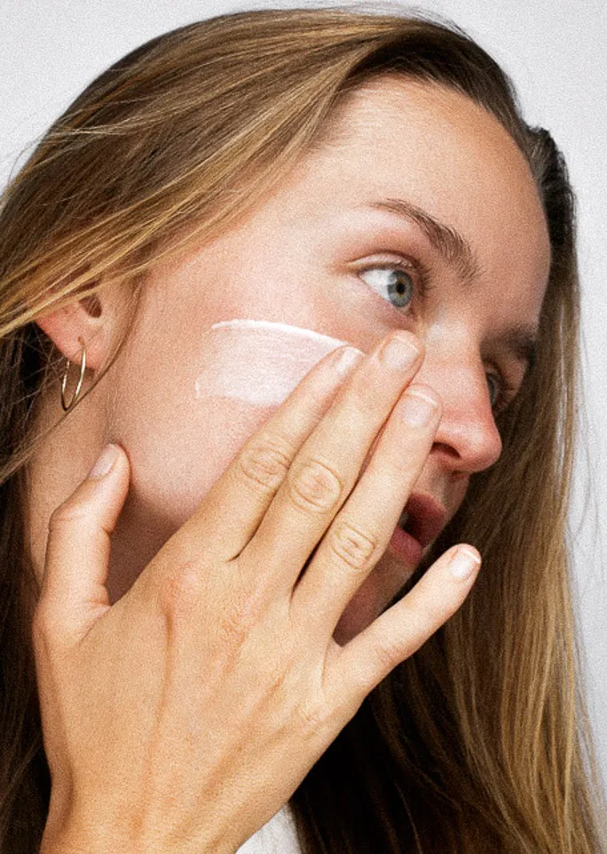 Žena si aplikuje krém na líce.