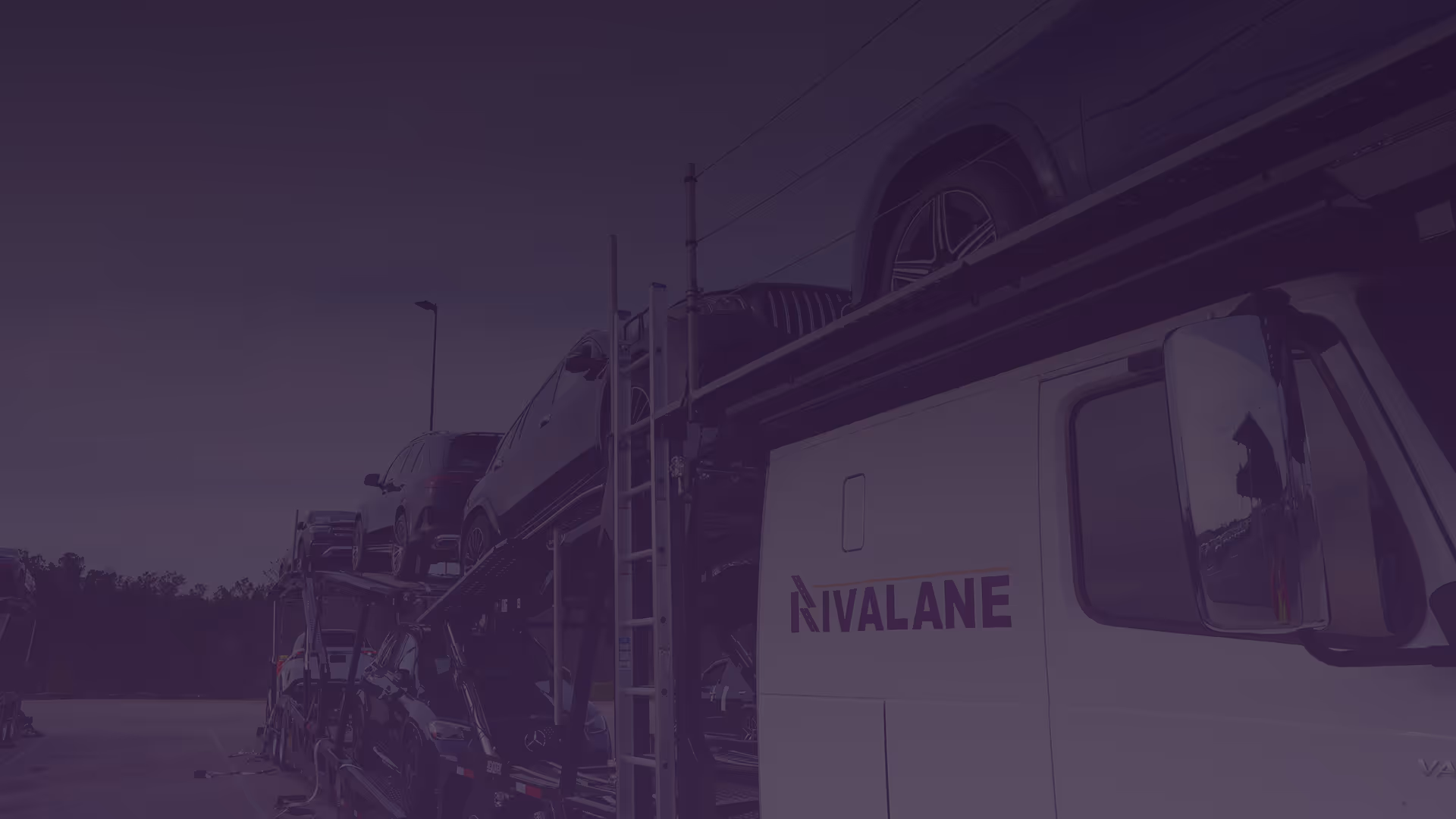 Car carrier truck loaded with multiple vehicles parked outdoors under a cloudy sky.