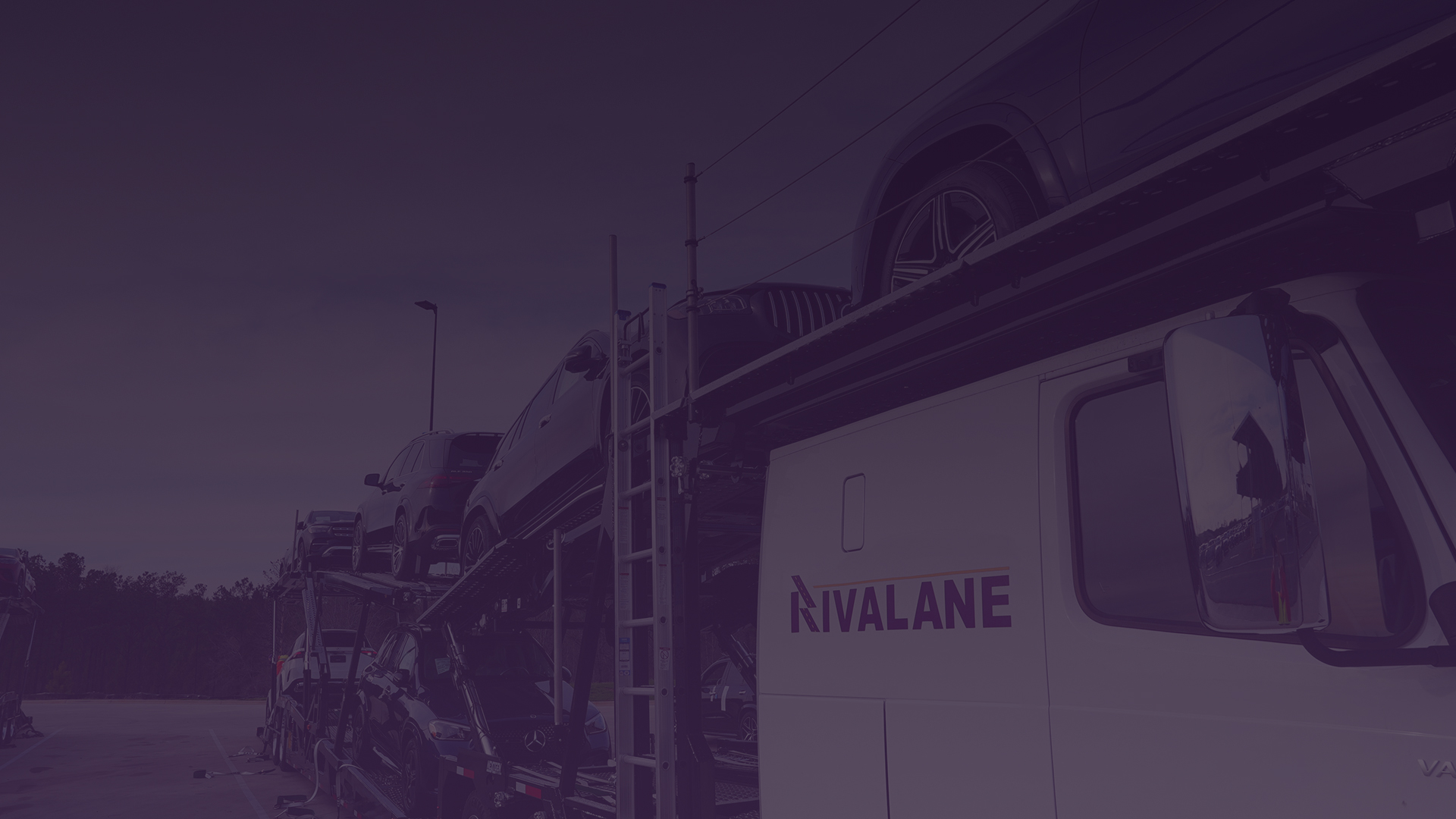 Car carrier truck loaded with multiple vehicles parked outdoors under a cloudy sky.