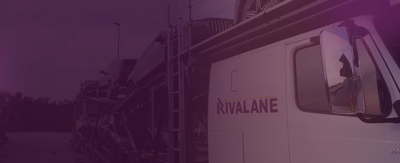 Car carrier truck with multiple cars loaded, parked outdoors near trees at dusk.