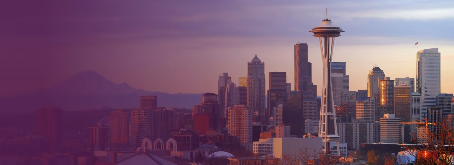 Seattle city skyline at sunset with the Space Needle and Mount Rainier in the background.
