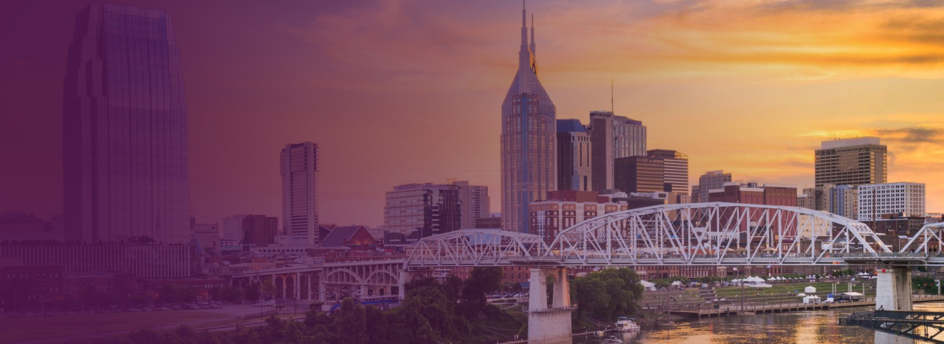 Skyline of Nashville, Tennessee at sunset with a prominent bridge over the river in the foreground.