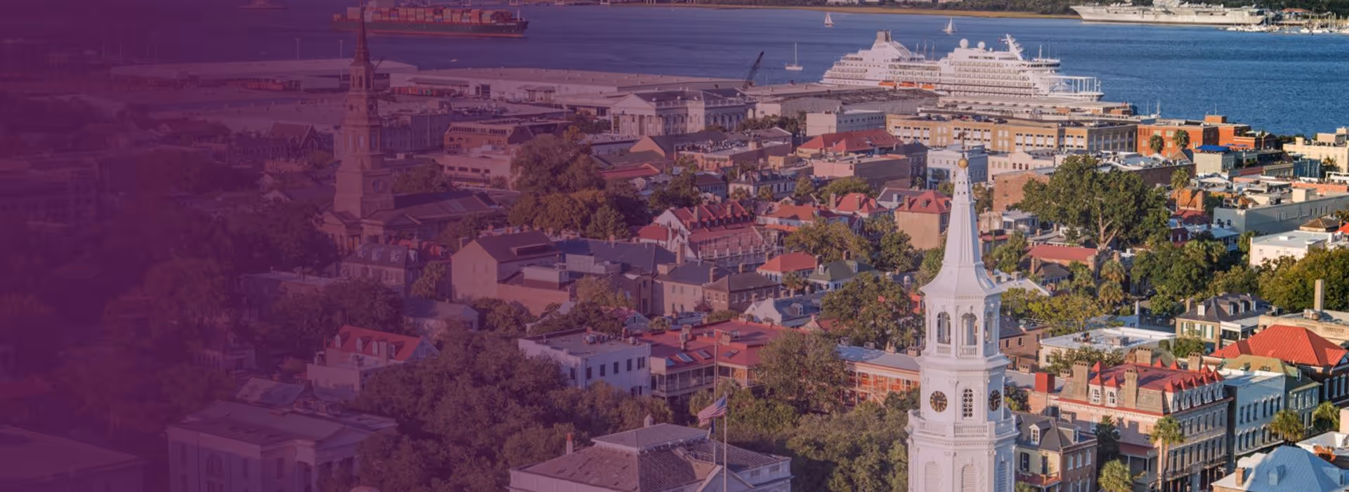 Aerial view of Charleston, South Carolina, featuring historic buildings, church steeples, and a cruise ship docked at the harbor.