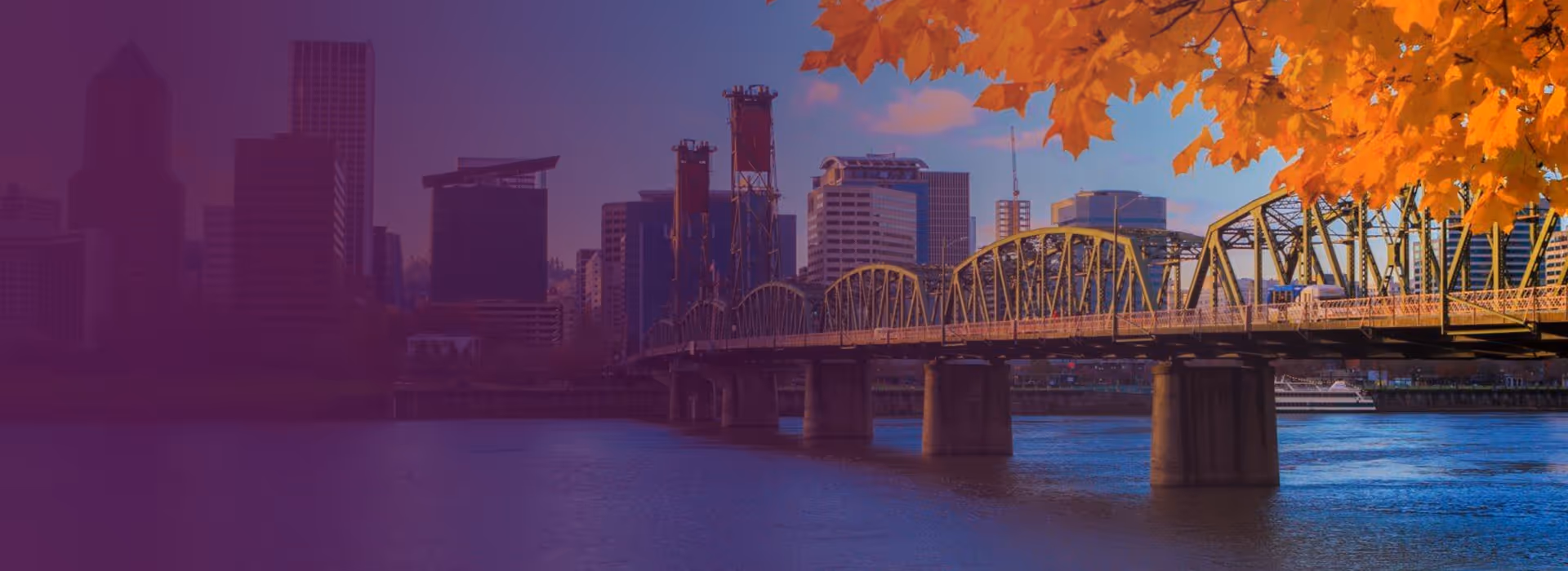 View of a city skyline with a yellow arched bridge over a river and autumn orange leaves in the foreground.